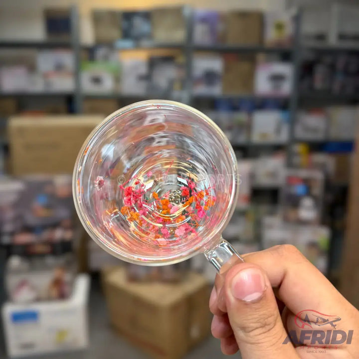 A clear glass mug with a scattering of colorful, tiny, dried flower petals at the bottom.