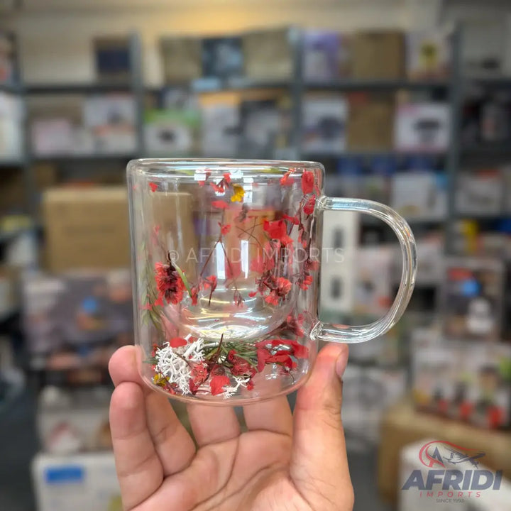 Double-walled glass mug with dried red flowers and white foliage embedded between layers.