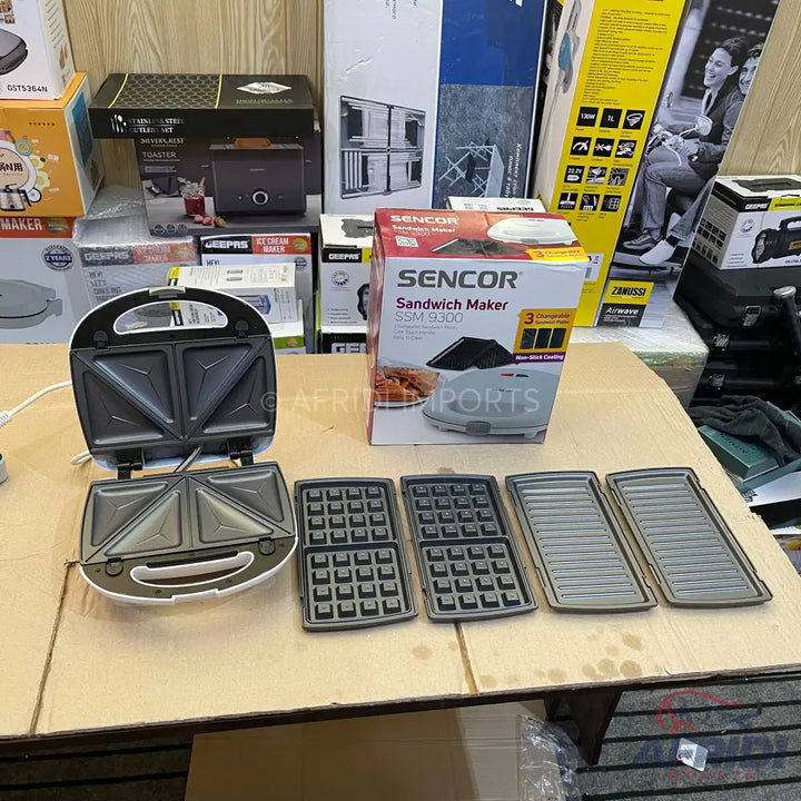 White Sencor sandwich maker with three sets of interchangeable plates for sandwiches, waffles, and grilling.