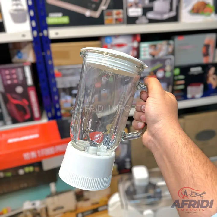 A clear glass blender jar with a white plastic base and lid, held by a hand.
