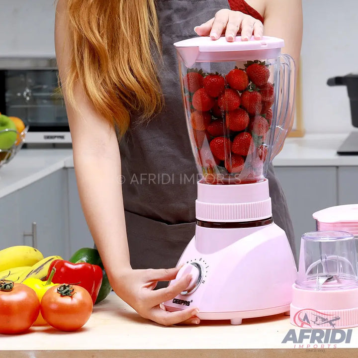Pink electric blender with a jar full of strawberries.