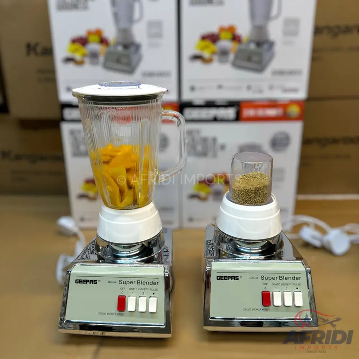 Two blenders, one with a large jar containing sliced mangoes and another with a smaller grinding attachment filled with seeds.