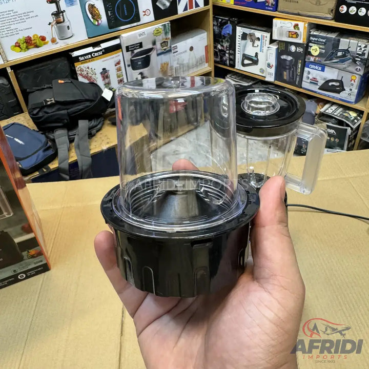 A clear plastic blender cup with a black base, held in a hand.