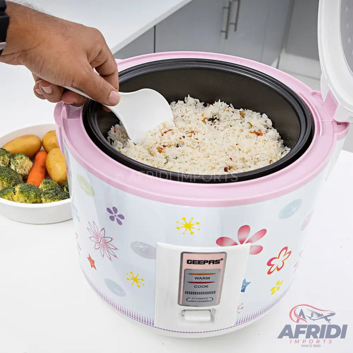 A floral-patterned pink and white rice cooker with cooked rice inside.