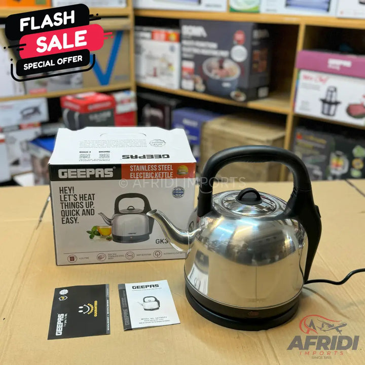 A stainless steel electric kettle with a black handle and base, accompanied by its packaging and instruction manuals.