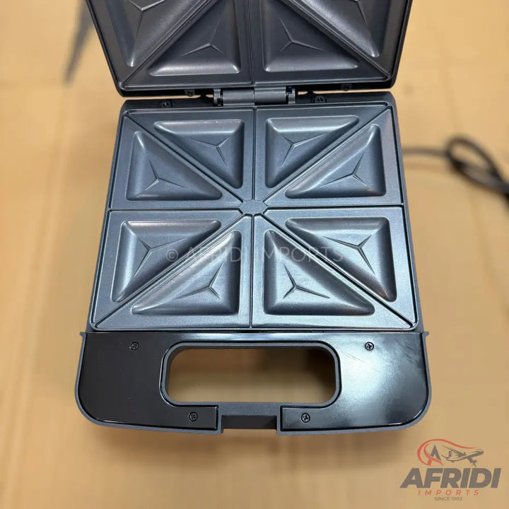 An open, dark grey sandwich maker with four triangular compartments.