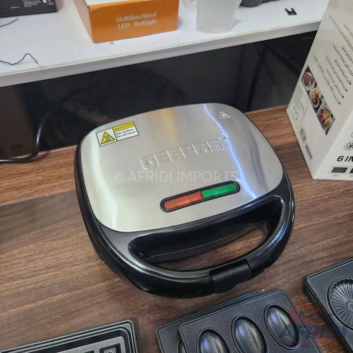 A silver and black electric waffle maker with interchangeable plates.