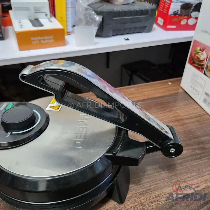 A round, silver and black electric tortilla or roti maker with a black handle and a dial for temperature control.