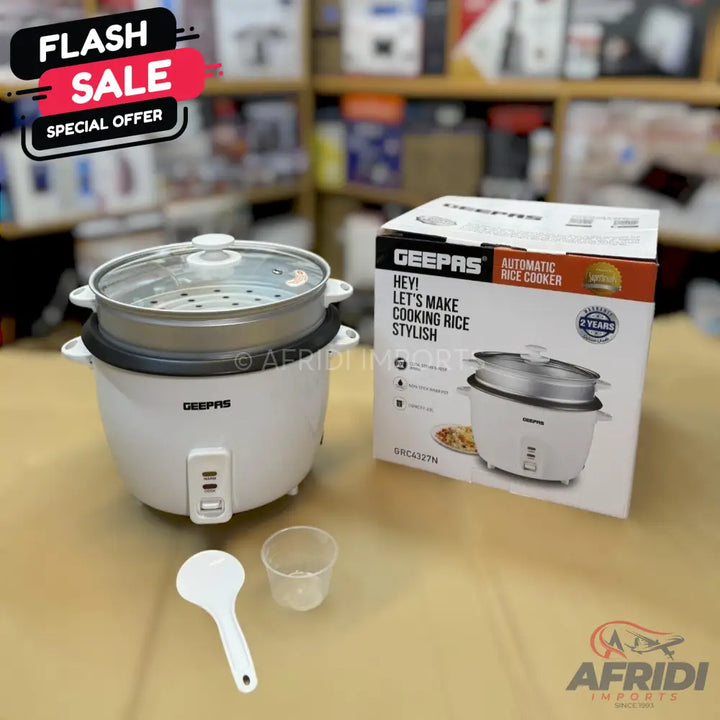 White Geepas automatic rice cooker with a steamer basket and glass lid, accompanied by a rice paddle and measuring cup.