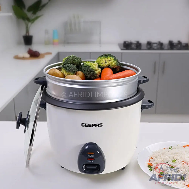 White electric rice cooker with a steaming basket full of vegetables.