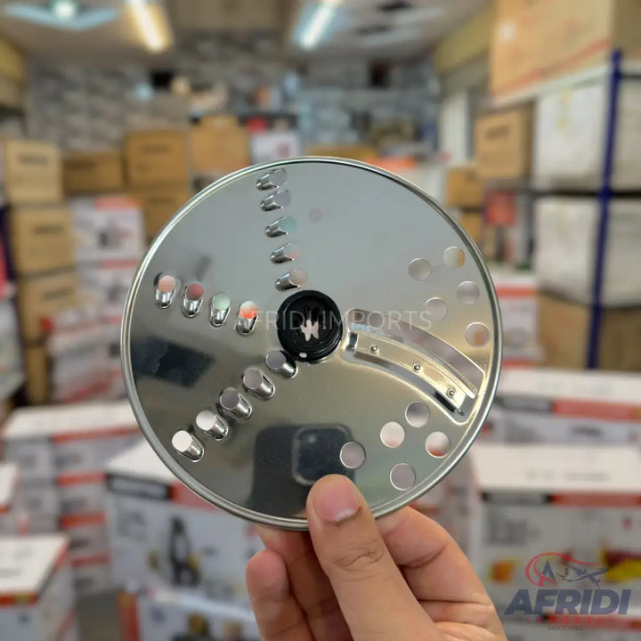 A stainless steel food processor disc with various shredding and slicing holes.