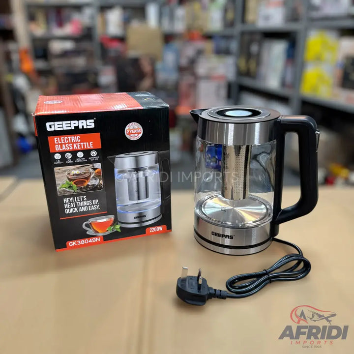 A glass electric kettle with a stainless steel base and infuser, accompanied by its packaging.