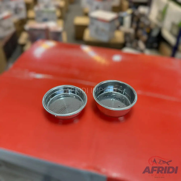 Two round, metallic, perforated coffee filter baskets.