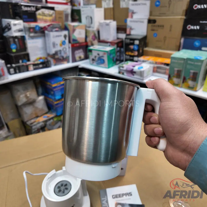 A stainless steel electric kettle or blender cup with a white handle and base.