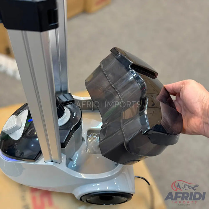 A white and black garment steamer with a removable water tank being held by a hand.