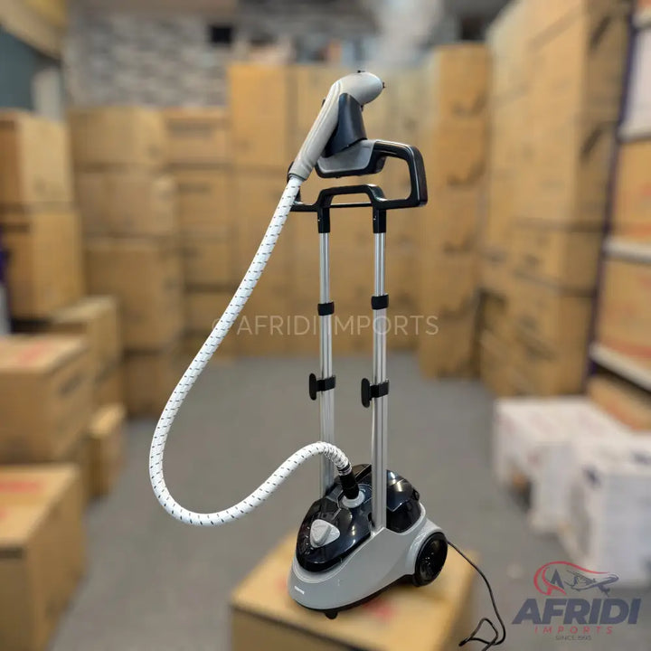 A floor-standing garment steamer with a white hose and a grey and black base.