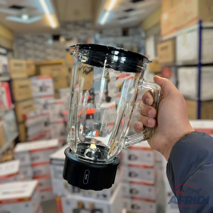Glass blender jar with a black lid and base, held by a hand.