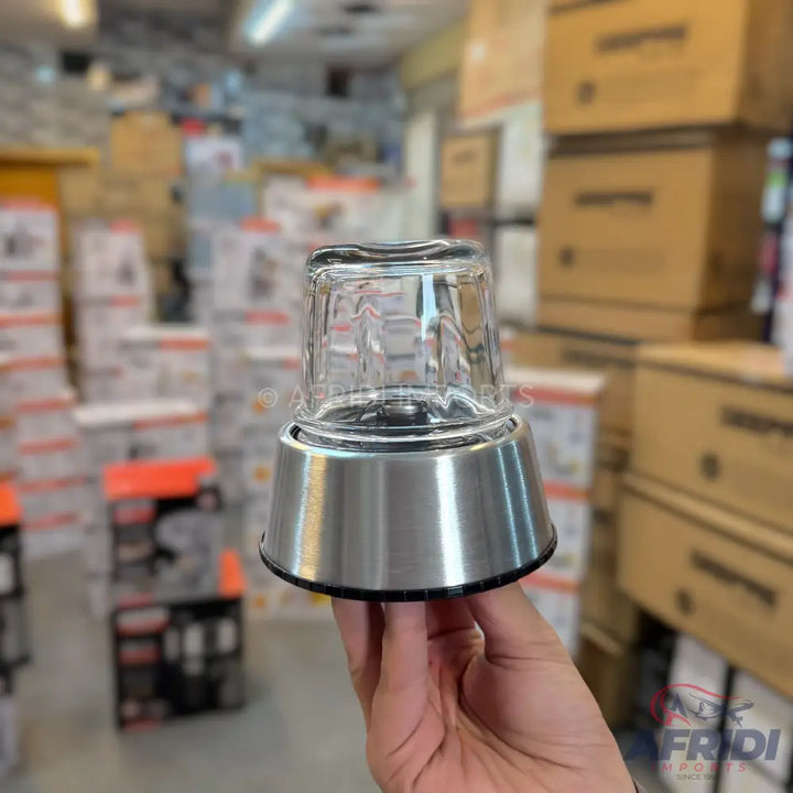 A hand holding a clear glass and stainless steel blender base.