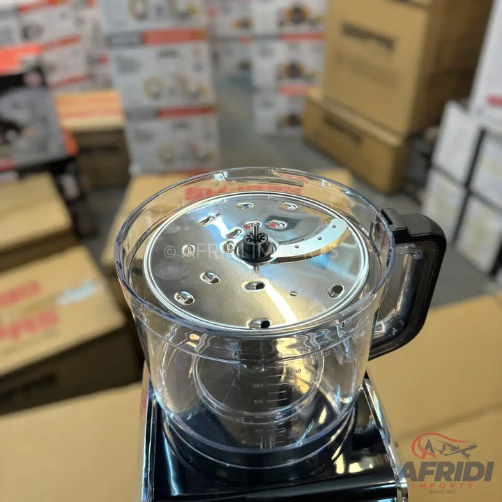A clear plastic food processor bowl with a metal slicing/shredding disc and a black handle.