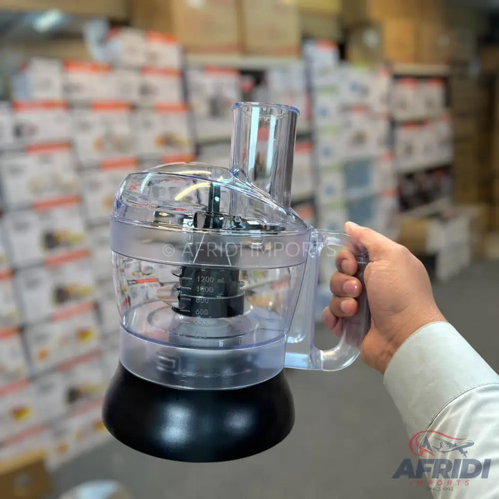 A clear plastic food processor with a black base and a handle, featuring measurement markings on the bowl.