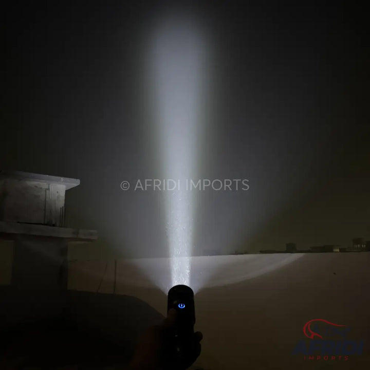 A black flashlight emitting a powerful beam of white light, with a blue power button illuminated.