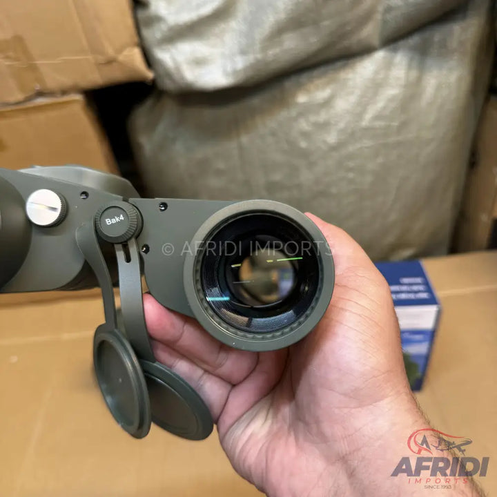 Dark green binoculars with attached lens caps, held in a hand.