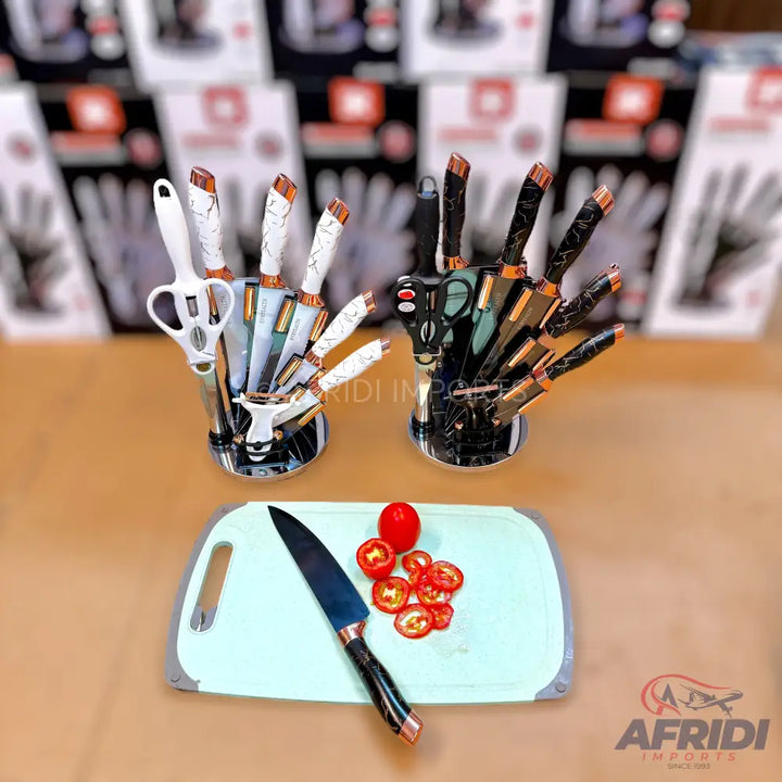 A set of white and black handled knives with matching scissors in two hand-shaped holders, with a single knife and sliced tomatoes on a cutting board in the foreground.