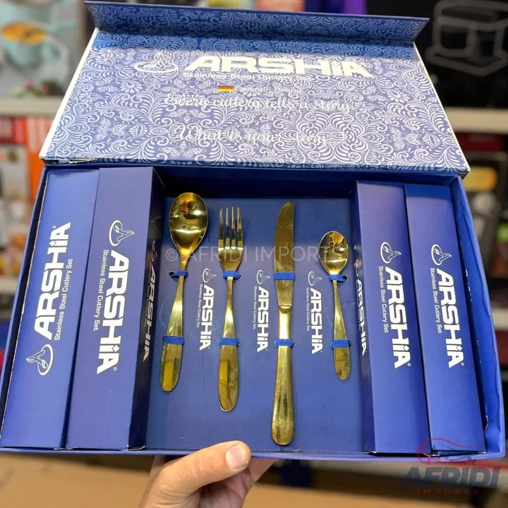 A boxed set of gold-colored stainless steel cutlery, including spoons, forks, and knives.