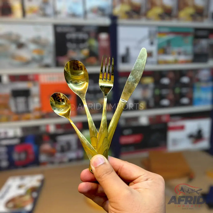 Four pieces of gold-colored stainless steel cutlery (two spoons, one fork, and one knife) held together in a hand.