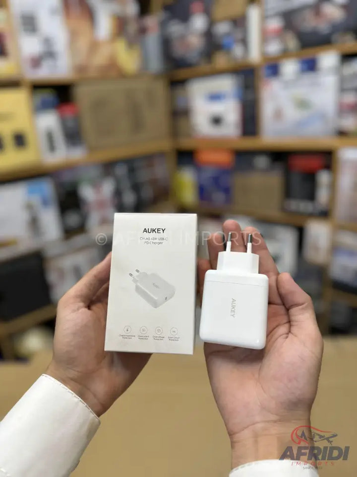 A white AUKEY branded wall charger with a two-pin European plug, held alongside its retail packaging.