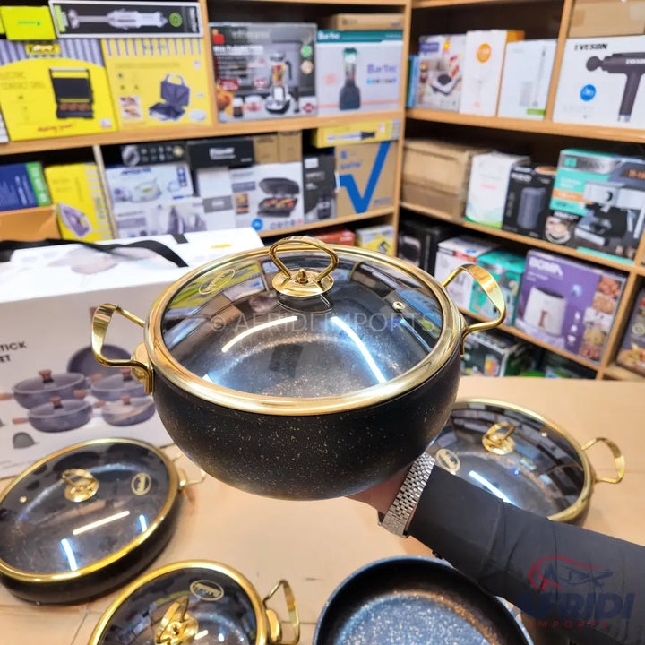 Black speckled cooking pot with gold-colored handles and a glass lid.