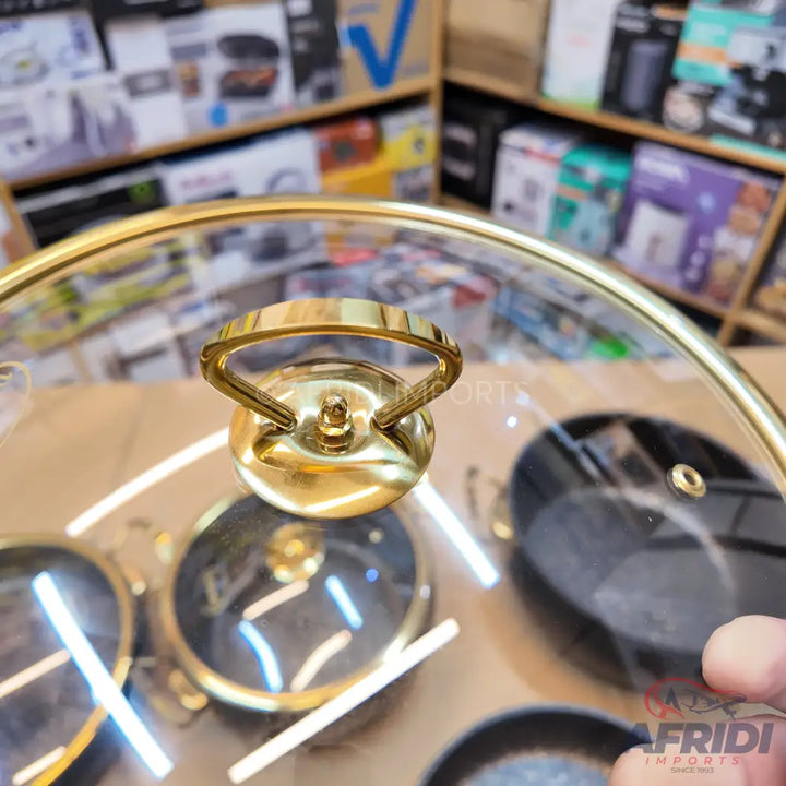 A clear glass pot lid with a golden rim and handle.