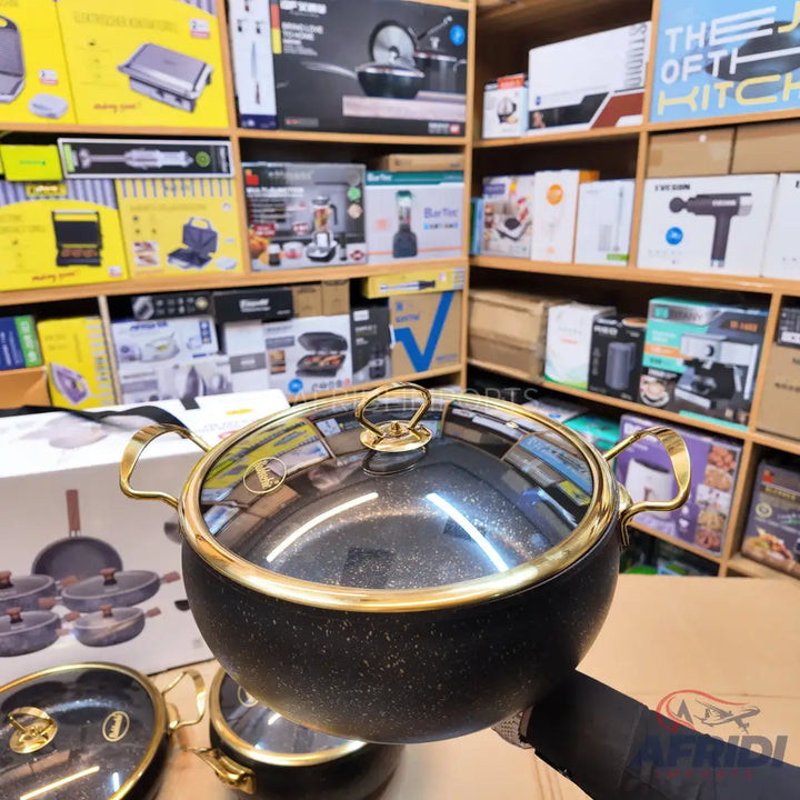 Black speckled cooking pot with gold-colored handles and rim, and a clear glass lid with a gold-colored knob.