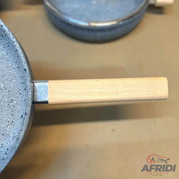 A frying pan with a speckled grey interior and a light wooden handle attached to a silver-colored metal bracket.