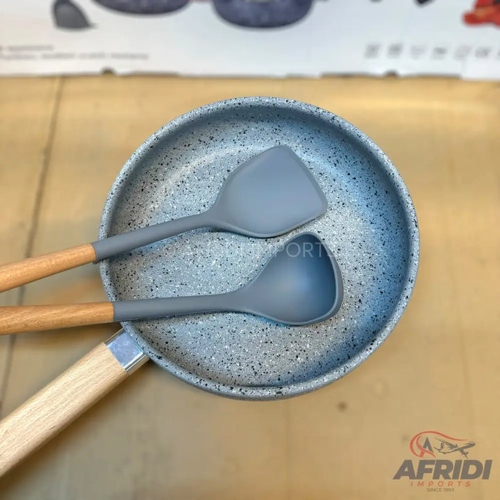 A non-stick frying pan with a wooden handle, accompanied by two grey silicone kitchen utensils with wooden handles.