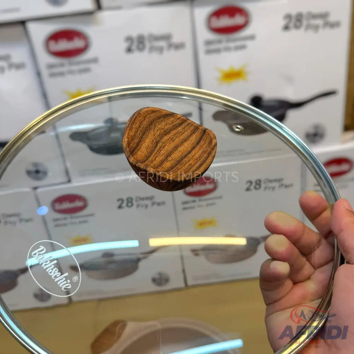 A clear glass lid with a wooden handle for a cooking pan.