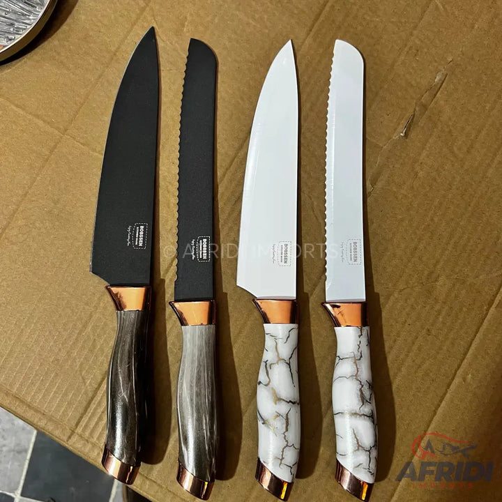 A set of four kitchen knives with two black and two white blades, each featuring rose gold accents on the bolster and end cap, and handles in either a dark wood-grain or white marble-like finish.