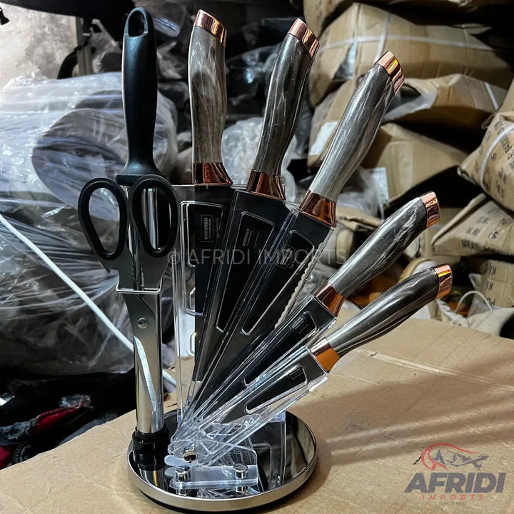 A set of six kitchen knives and a pair of scissors in a clear and metallic stand, featuring dark gray handles with copper-colored accents.