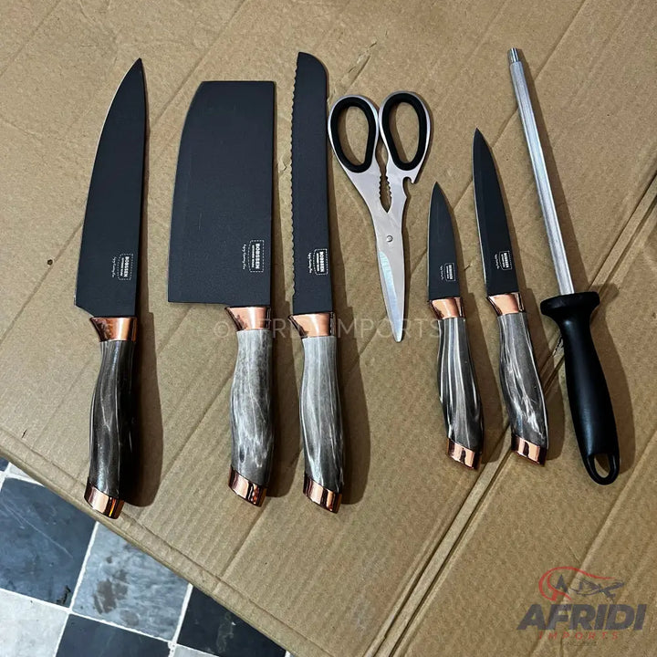 A set of black kitchen knives with gray and copper-colored handles, including a cleaver, a bread knife, two smaller knives, kitchen shears, and a sharpening steel.