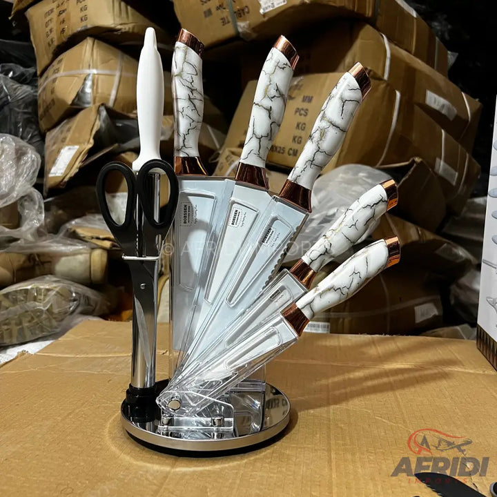A knife block with a set of knives featuring white marble-patterned handles with copper-colored accents, and a pair of black-handled scissors.