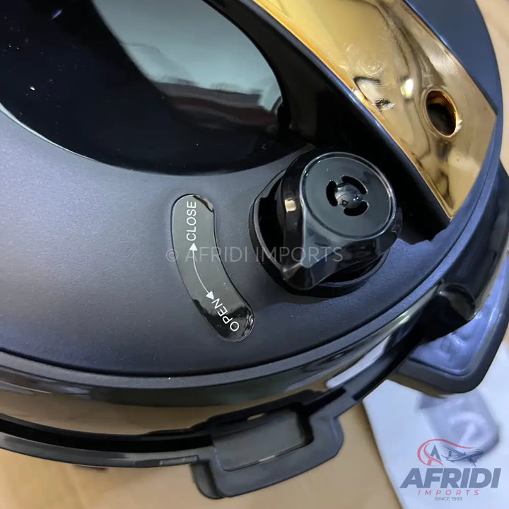 A black pressure cooker lid with a gold-colored accent and a clear open/close mechanism.