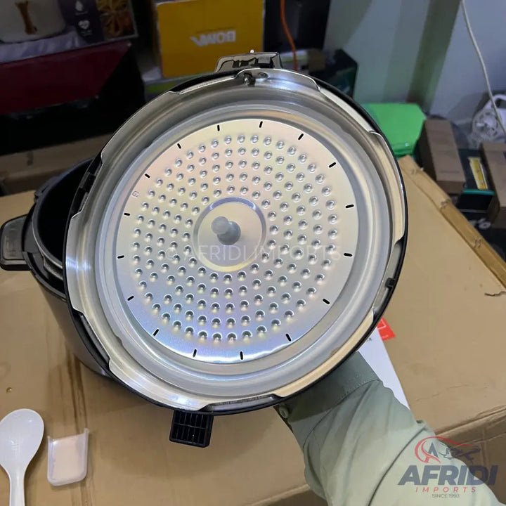An open electric pressure cooker with a textured silver inner lid and a black exterior.