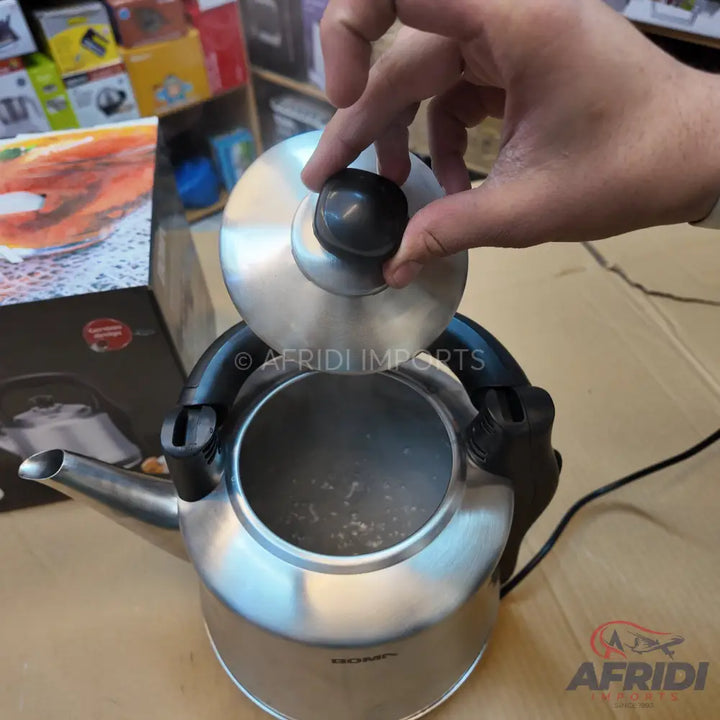Stainless steel electric kettle with a black handle and lid knob, with steam rising from the opening.