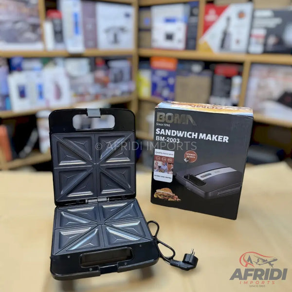 An open black electric sandwich maker with two square cooking plates, each divided into two triangular sections, and its product box.