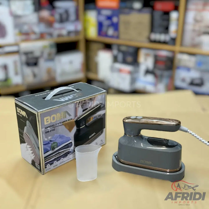 A gray and gold handheld steam iron with its original packaging and a measuring cup.