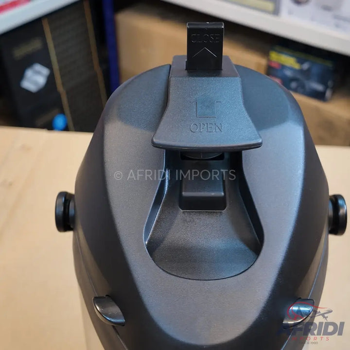 A close-up view of the top portion of a dark gray thermal carafe, featuring a push-button pour spout and a slide lock mechanism to toggle between ’OPEN’ and ’CLOSE.’