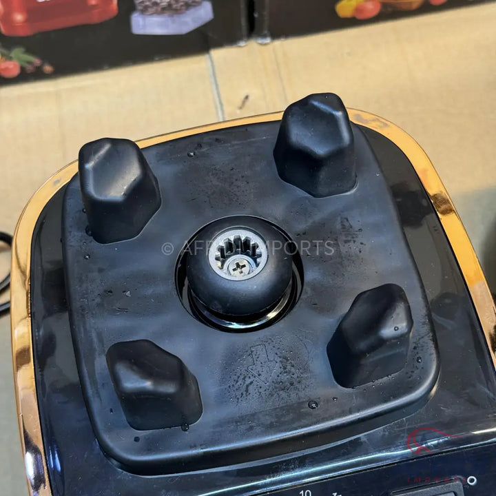 The top of a black and gold blender base, featuring a drive socket with a visible screw and four rubber feet for stabilization.