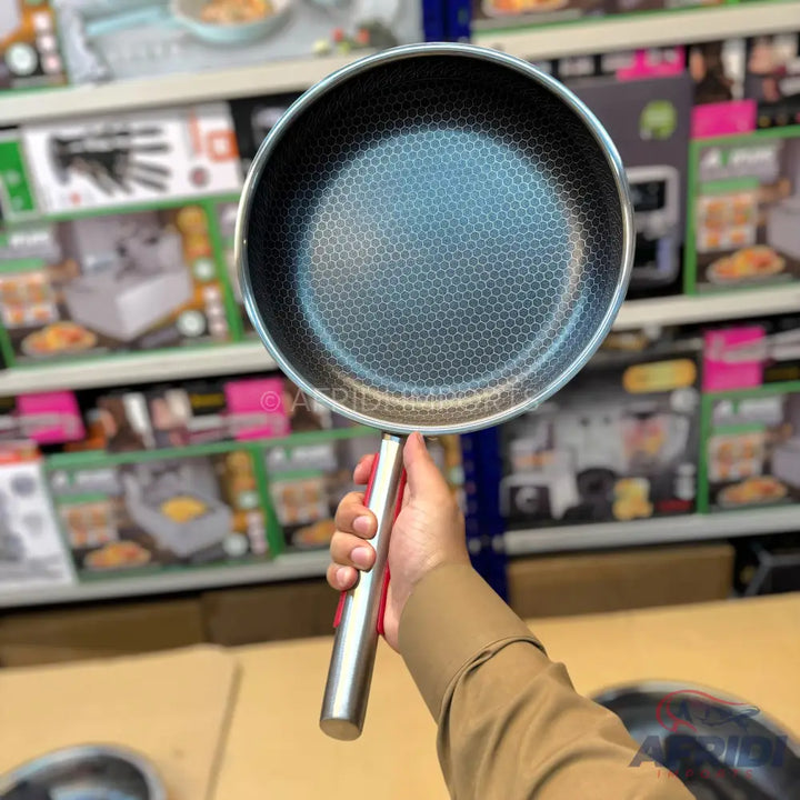 A person holding a stainless steel frying pan with a honeycomb pattern non-stick surface.