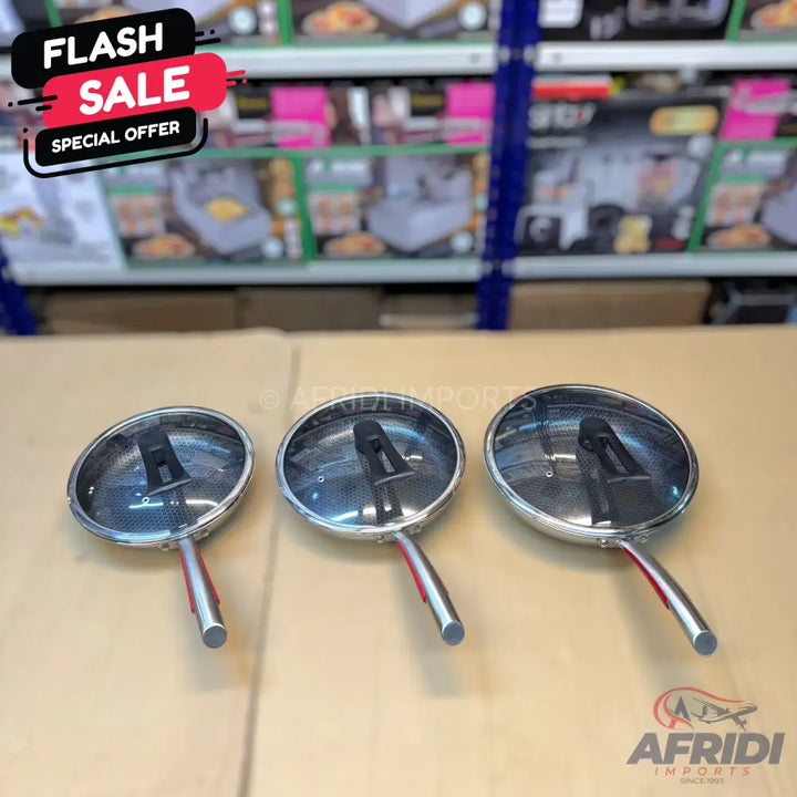Set of three stainless steel frying pans with glass lids and red handles.