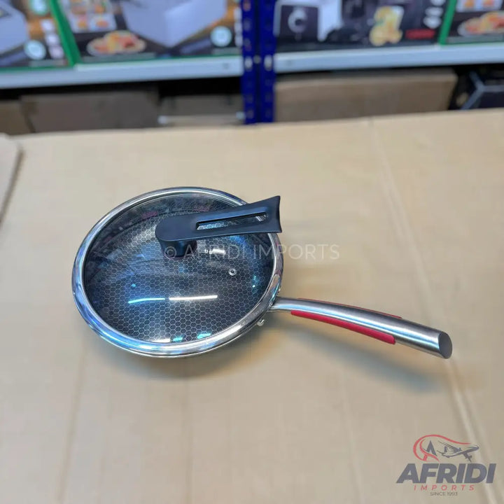 Stainless steel frying pan with a glass lid and a red-accented handle.
